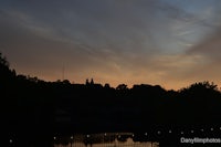 sunset over a river with trees and buildings in the background
