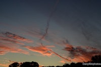 a sunset with clouds and a contrail in the sky